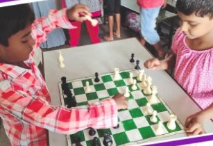 Two children playing chess on a green board
